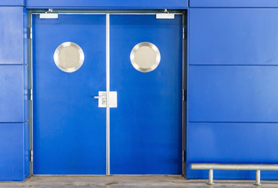 Blue double swing doors with round windows and overhead closers